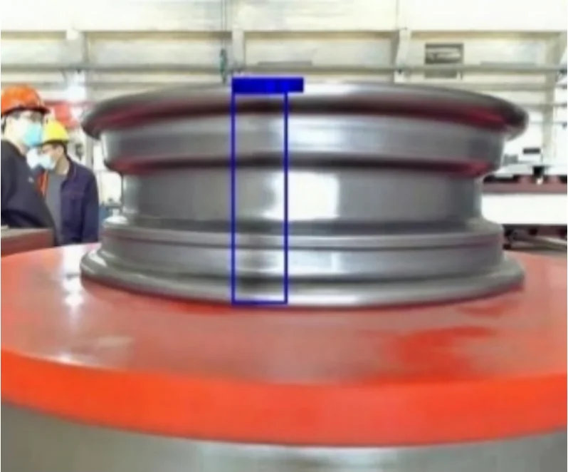 A steel wheel hub on an inspection table, with the detected weld seam marked by a blue bounding box